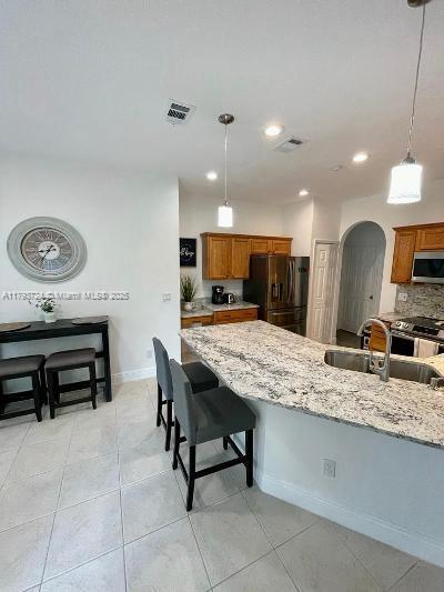 kitchen featuring brown cabinets, a kitchen bar, stainless steel appliances, pendant lighting, and backsplash