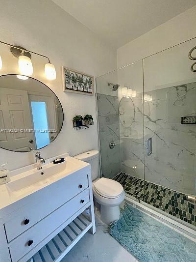 full bath with toilet, a marble finish shower, and vanity