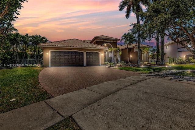mediterranean / spanish-style house with an attached garage, stucco siding, a tile roof, a lawn, and decorative driveway