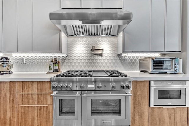 kitchen with tasteful backsplash, a toaster, light countertops, range hood, and appliances with stainless steel finishes