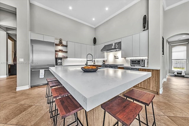 kitchen featuring a sink, wall chimney exhaust hood, built in refrigerator, a high ceiling, and modern cabinets