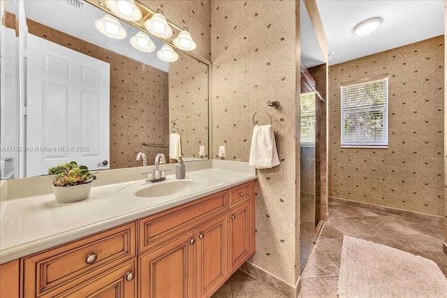 bathroom featuring wallpapered walls, baseboards, tile patterned flooring, tiled shower, and vanity