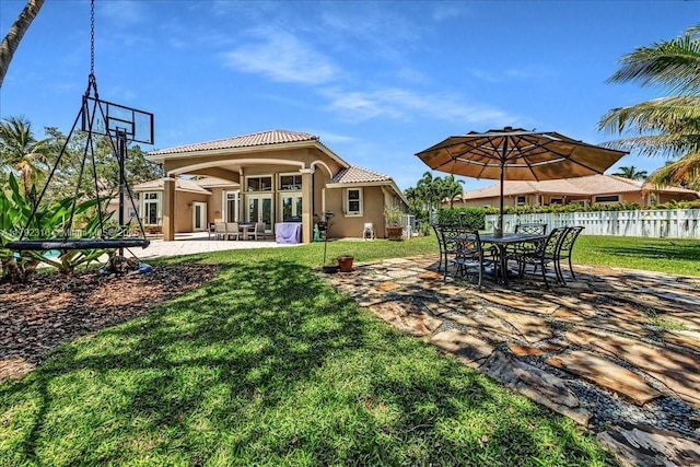 rear view of house featuring a patio, stucco siding, a tile roof, fence, and a lawn