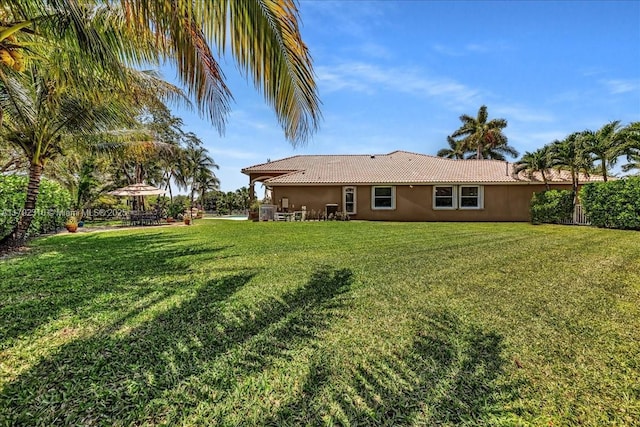 back of property featuring a tile roof, stucco siding, and a yard