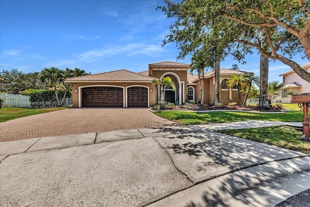 mediterranean / spanish-style house featuring a tiled roof, decorative driveway, an attached garage, stucco siding, and a front yard