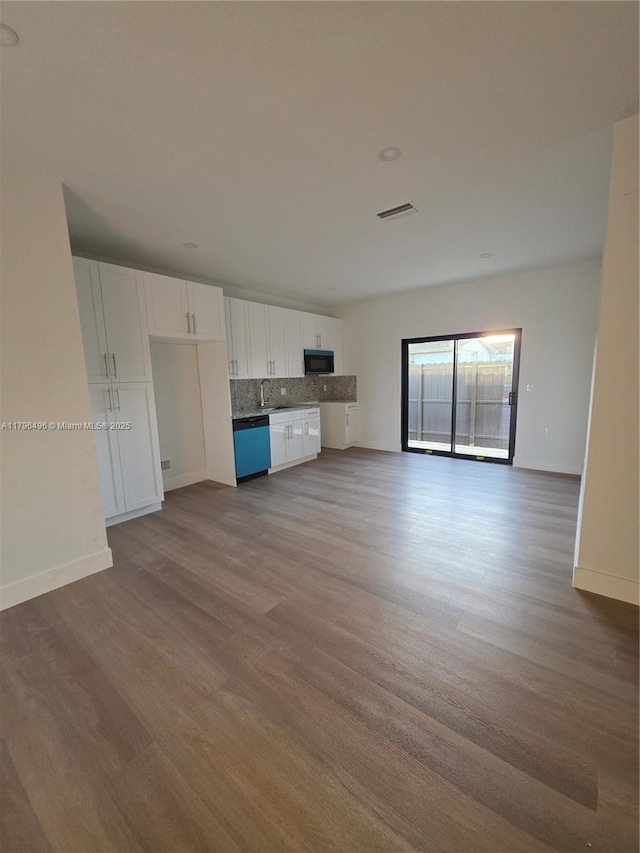 unfurnished living room with wood finished floors, visible vents, baseboards, and a sink
