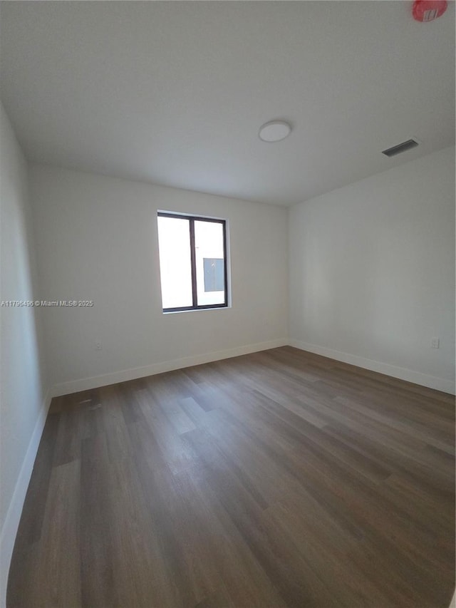 unfurnished room with baseboards, visible vents, and dark wood-type flooring