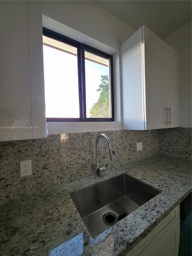 kitchen featuring white cabinetry, light stone counters, tasteful backsplash, and a sink