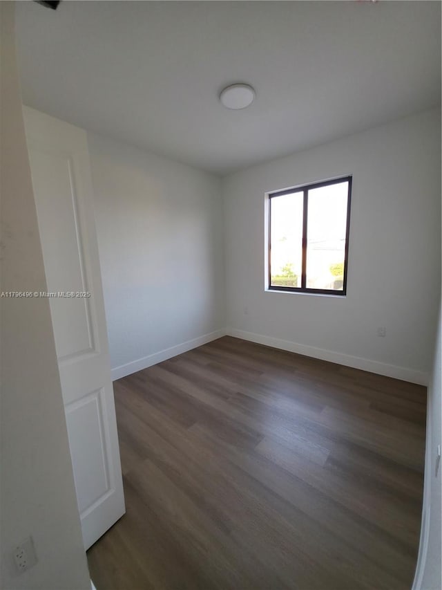 spare room featuring dark wood-style flooring and baseboards