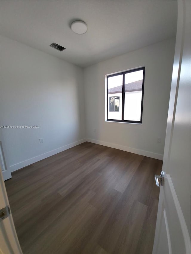 spare room featuring baseboards, dark wood-type flooring, and visible vents