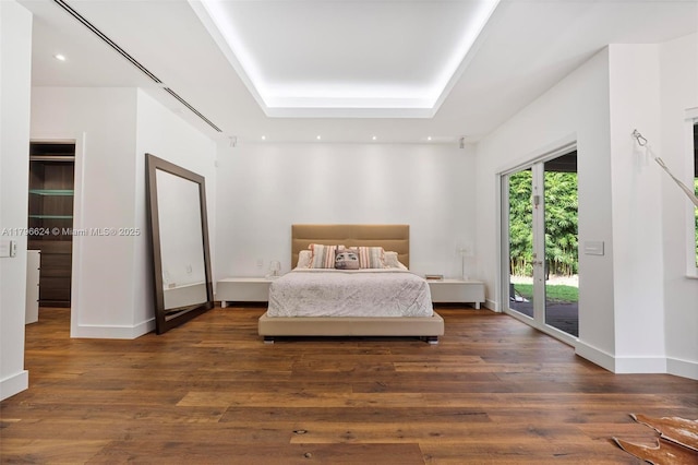 bedroom with a tray ceiling, access to outside, wood finished floors, and recessed lighting