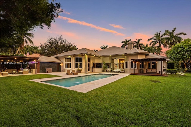 back of house at dusk with an outdoor hangout area, a chimney, a patio area, and an outdoor pool