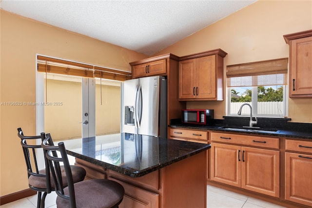 kitchen with a breakfast bar area, stainless steel fridge, light tile patterned floors, a sink, and vaulted ceiling