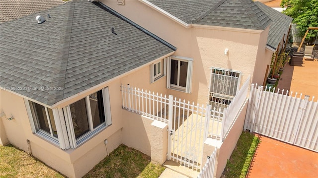 view of property exterior with stucco siding, roof with shingles, and fence