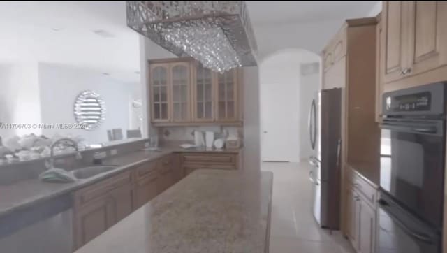 kitchen featuring glass insert cabinets, a sink, freestanding refrigerator, cream cabinetry, and dobule oven black