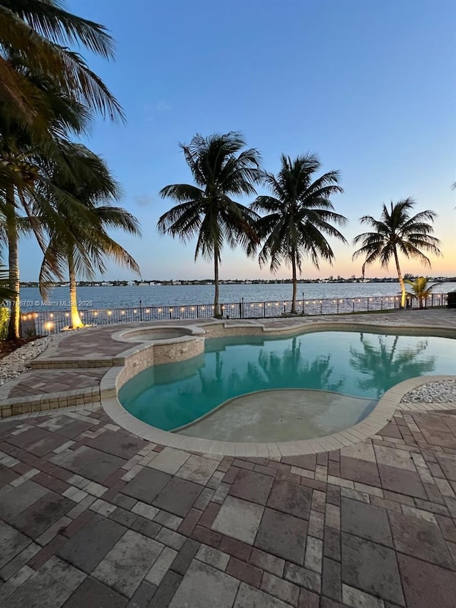 pool at dusk with a water view, a patio, and a fenced in pool