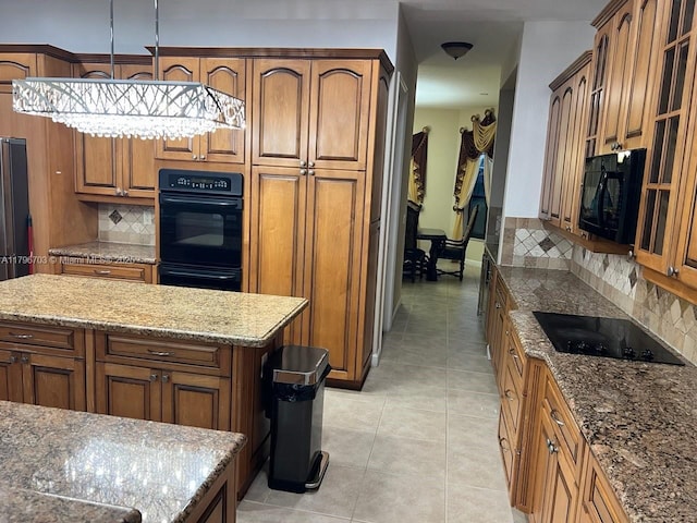 kitchen with light stone countertops, light tile patterned flooring, brown cabinets, decorative backsplash, and black appliances