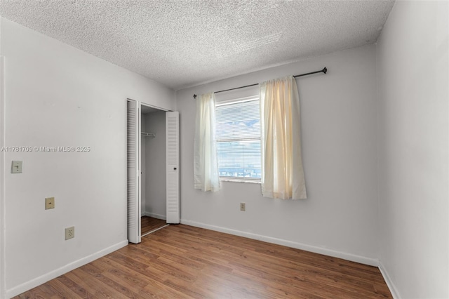 unfurnished bedroom featuring baseboards, a closet, a textured ceiling, and wood finished floors
