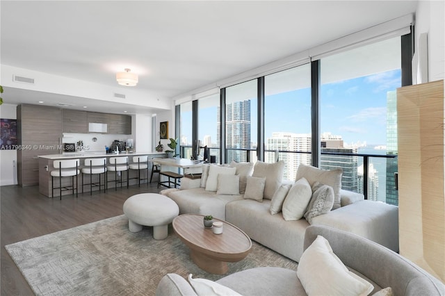 living area with floor to ceiling windows, visible vents, wood finished floors, and a view of city