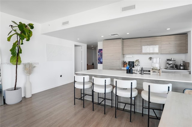 kitchen with modern cabinets, a breakfast bar area, visible vents, and wood finished floors