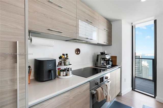 kitchen with expansive windows, modern cabinets, black electric cooktop, light wood-style floors, and stainless steel oven