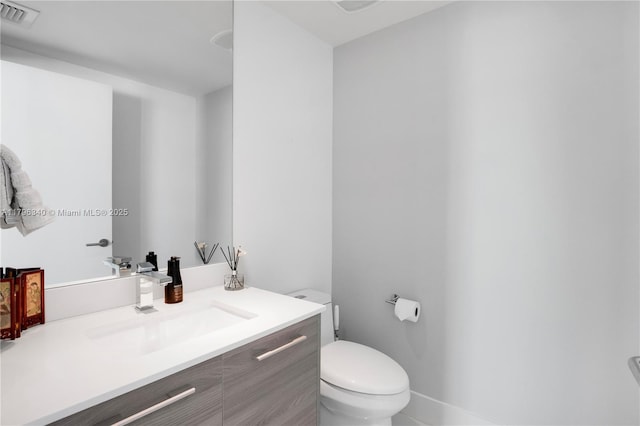 bathroom with toilet, vanity, and visible vents