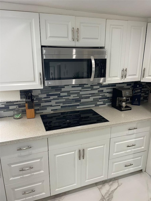 493 Camino Real Blvd, Clewiston, FL 33440 - kitchen featuring backsplash, black electric stovetop, white cabinets, and stainless steel microwave