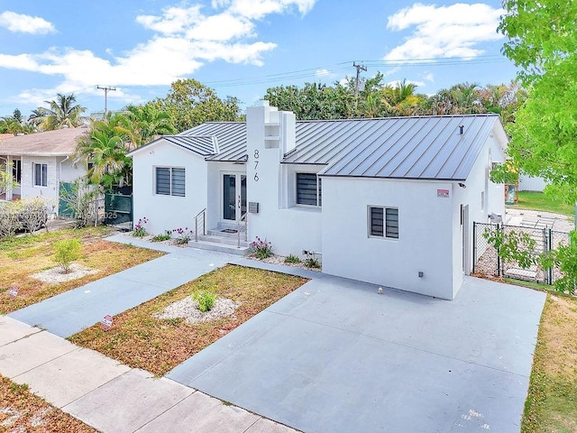 view of front of property featuring metal roof, a standing seam roof, stucco siding, and a gate