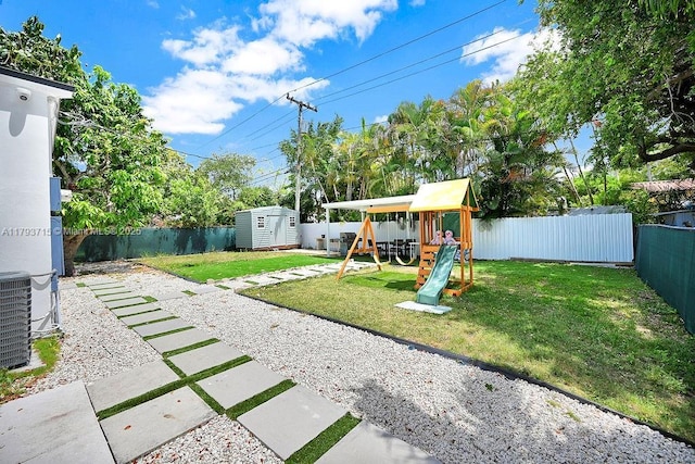 view of yard featuring a storage shed, a playground, an outdoor structure, central AC unit, and a fenced backyard