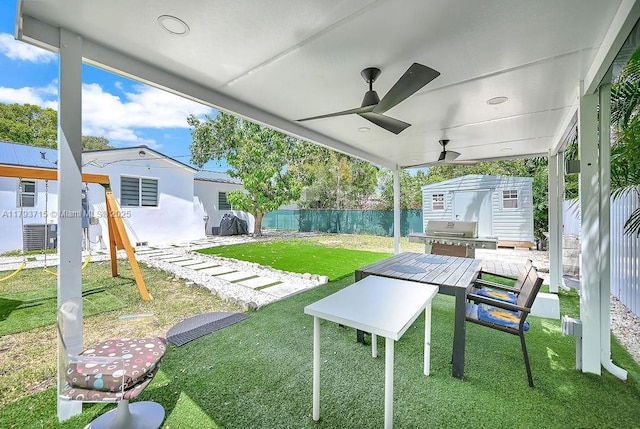 view of yard featuring a ceiling fan, outdoor dining space, an outdoor structure, a fenced backyard, and a storage unit