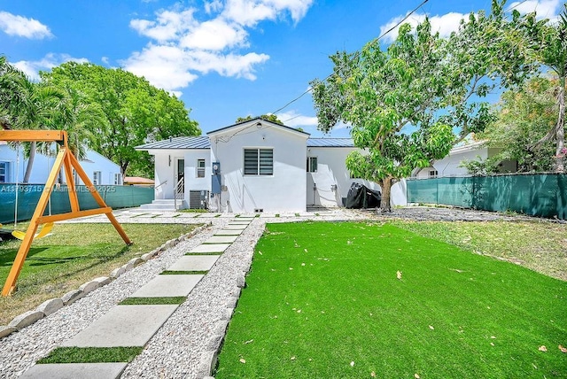 rear view of property with fence, a playground, stucco siding, and a standing seam roof