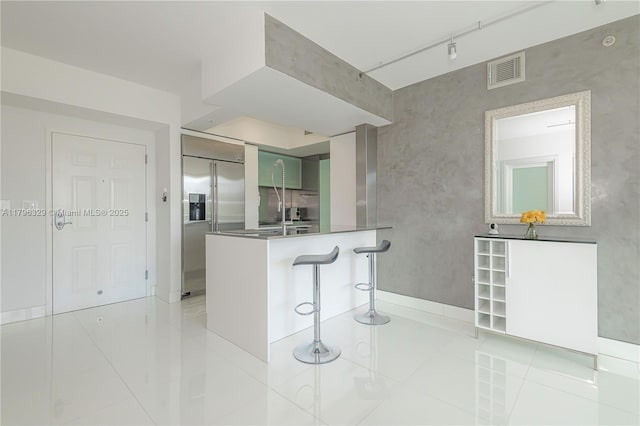 kitchen featuring stainless steel built in refrigerator, light tile patterned floors, visible vents, a peninsula, and a kitchen breakfast bar