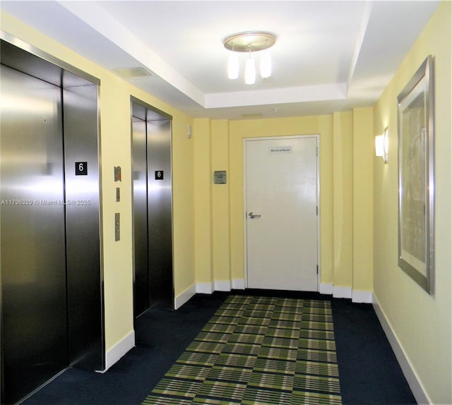 interior space with elevator, dark colored carpet, and a raised ceiling
