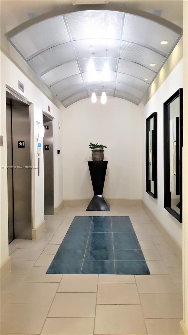 corridor with vaulted ceiling, baseboards, elevator, and tile patterned floors