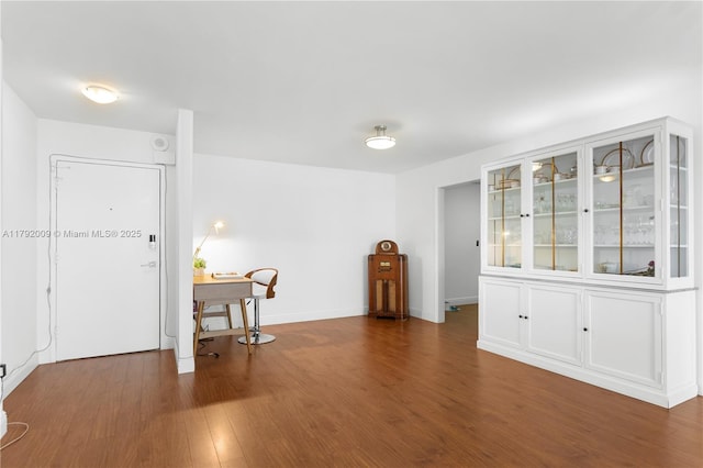 unfurnished room featuring dark wood-style floors, baseboards, and an office area