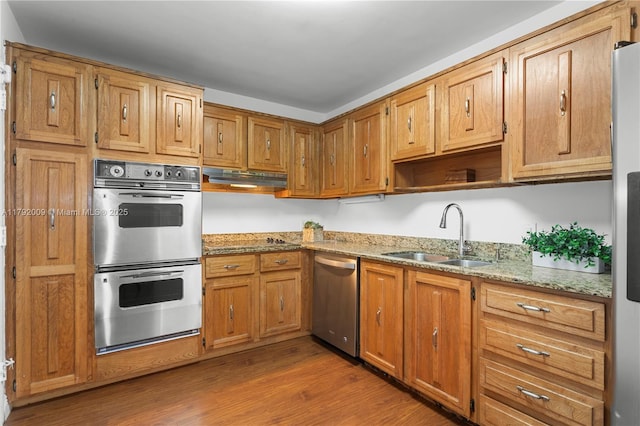 kitchen featuring stainless steel appliances, a sink, wood finished floors, under cabinet range hood, and light stone countertops
