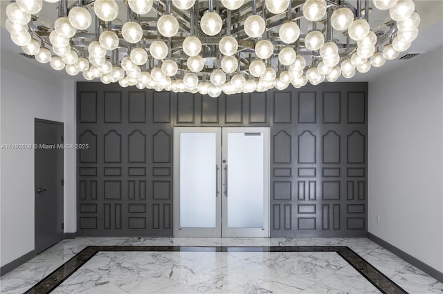 entrance foyer with marble tiled flooring, inlaid floor details, a chandelier, and baseboards