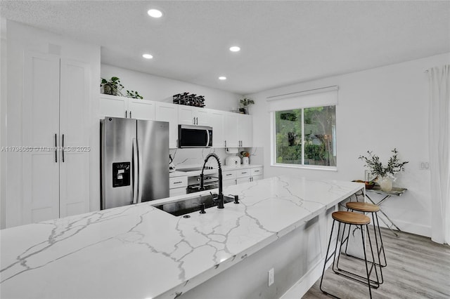 kitchen with light wood-style floors, white cabinetry, light stone countertops, appliances with stainless steel finishes, and recessed lighting