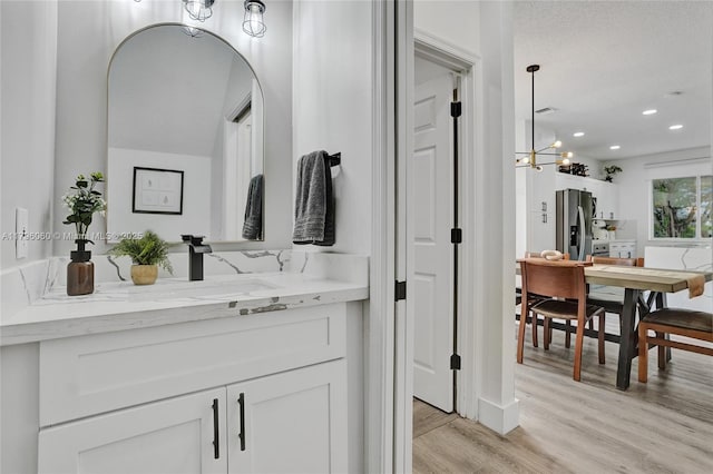 bathroom with vanity, an inviting chandelier, recessed lighting, and wood finished floors