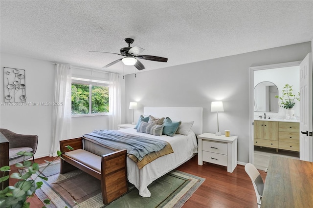bedroom featuring a ceiling fan, a textured ceiling, ensuite bathroom, a sink, and wood finished floors