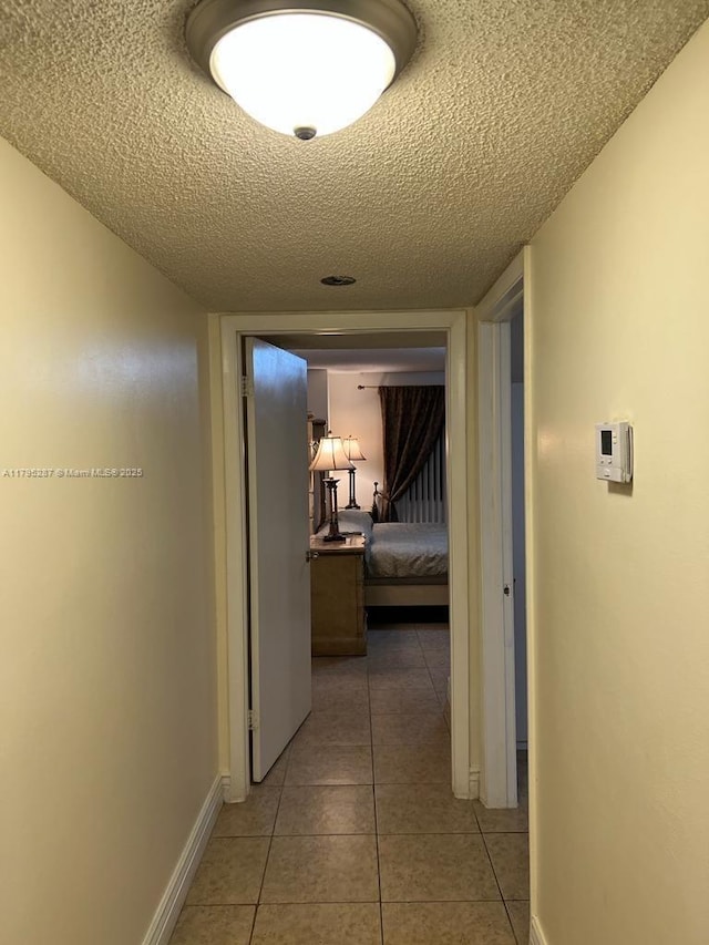 hall featuring baseboards, light tile patterned flooring, and a textured ceiling