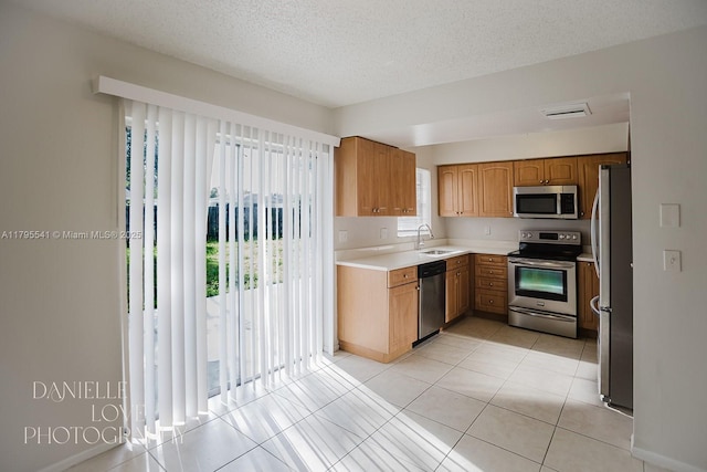 kitchen with a sink, brown cabinetry, a textured ceiling, light countertops, and appliances with stainless steel finishes