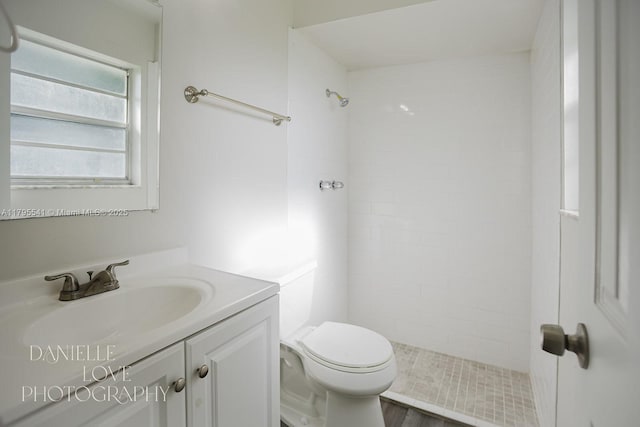 bathroom featuring a tile shower, vanity, and toilet