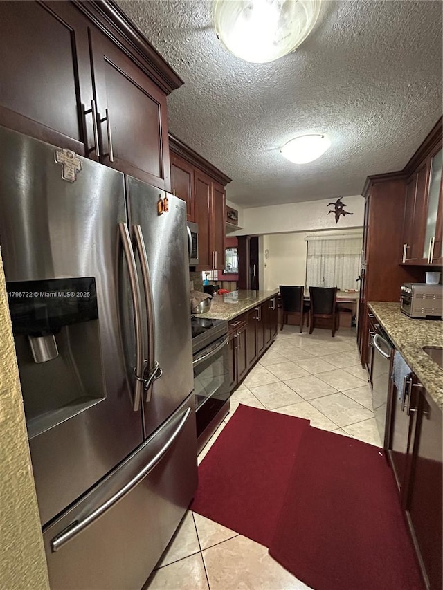kitchen with light tile patterned floors, dark brown cabinetry, a textured ceiling, light stone countertops, and appliances with stainless steel finishes