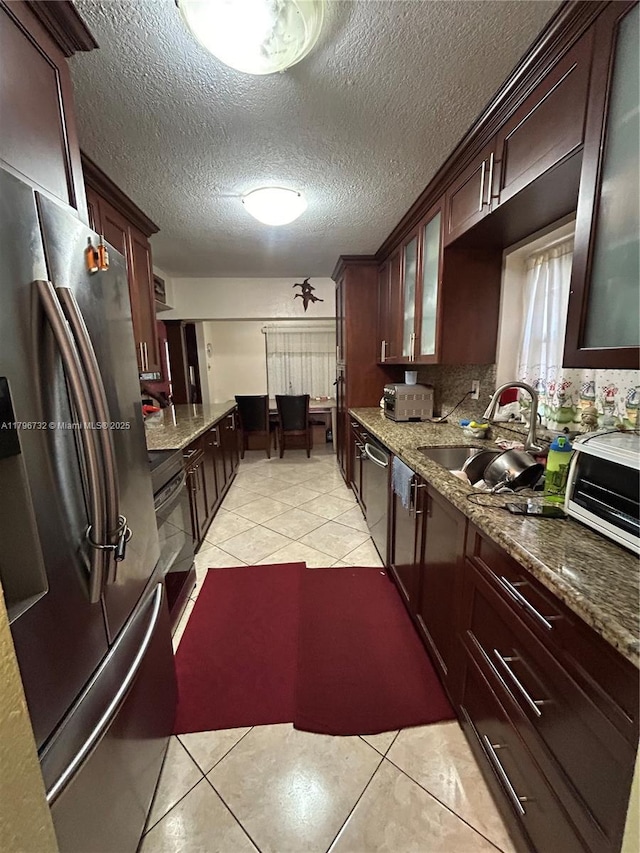 kitchen with stone countertops, glass insert cabinets, light tile patterned floors, a sink, and stainless steel appliances