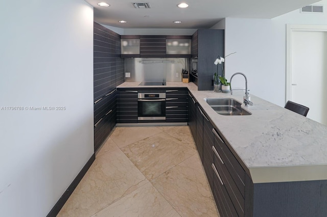 200 S Biscayne Blvd Unit 3903, Miami, FL 33131 - kitchen with oven, a peninsula, black electric stovetop, light stone counters, and dark cabinetry