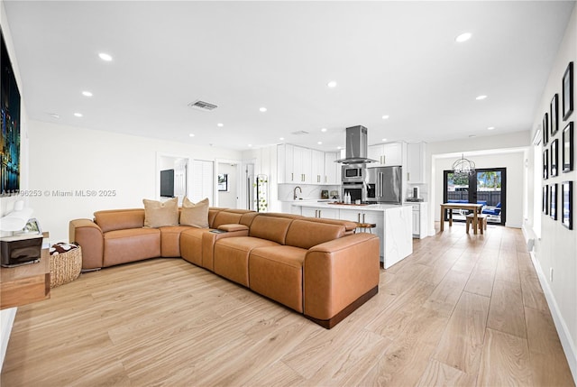 living area with an inviting chandelier, light wood-type flooring, visible vents, and recessed lighting
