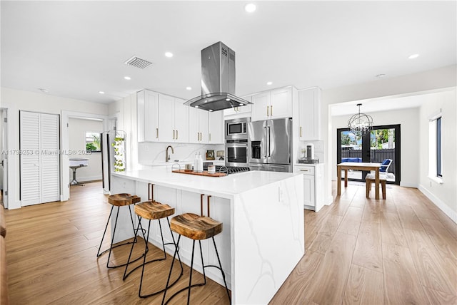 kitchen featuring a peninsula, island exhaust hood, a kitchen breakfast bar, visible vents, and appliances with stainless steel finishes
