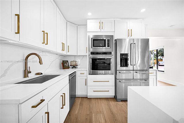 kitchen featuring light wood-style floors, stainless steel appliances, white cabinets, and a sink