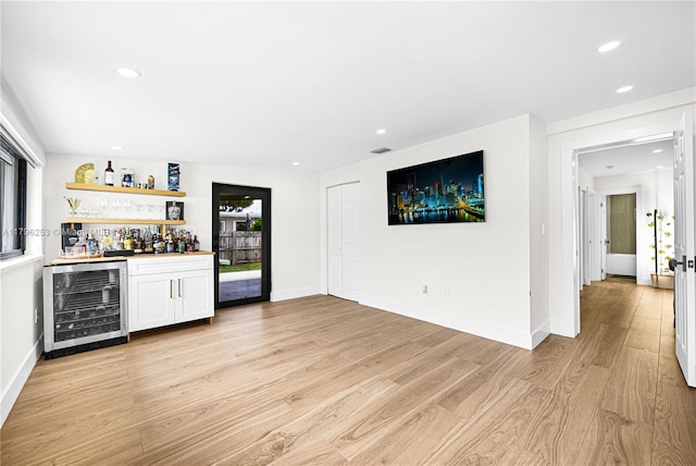 bar with a bar, light wood-type flooring, recessed lighting, and beverage cooler